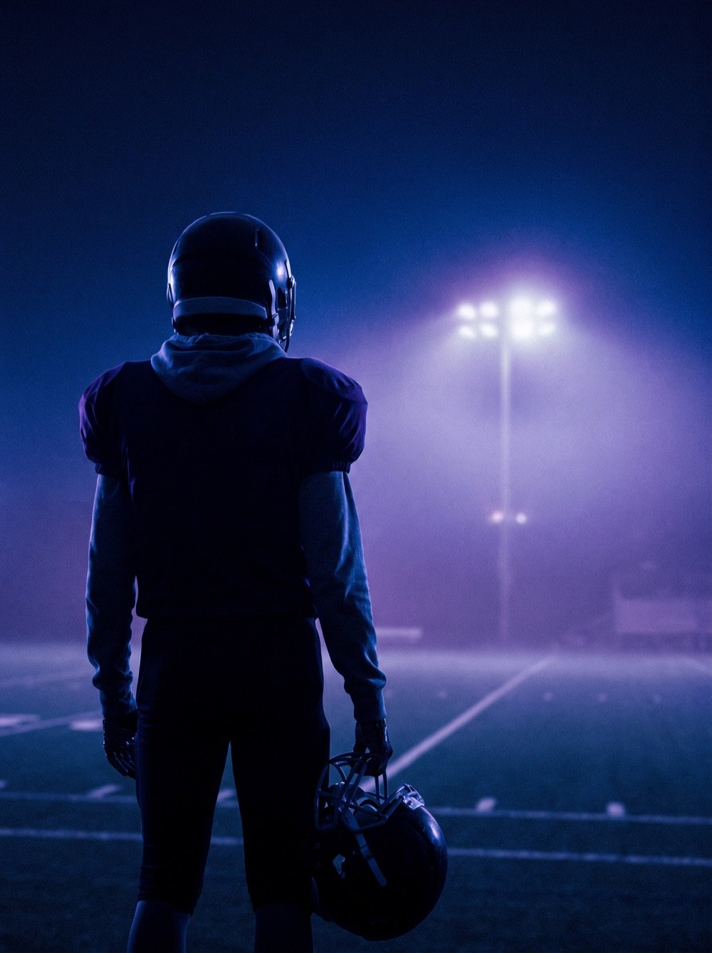 Silhouette of a young football player under stadium lights